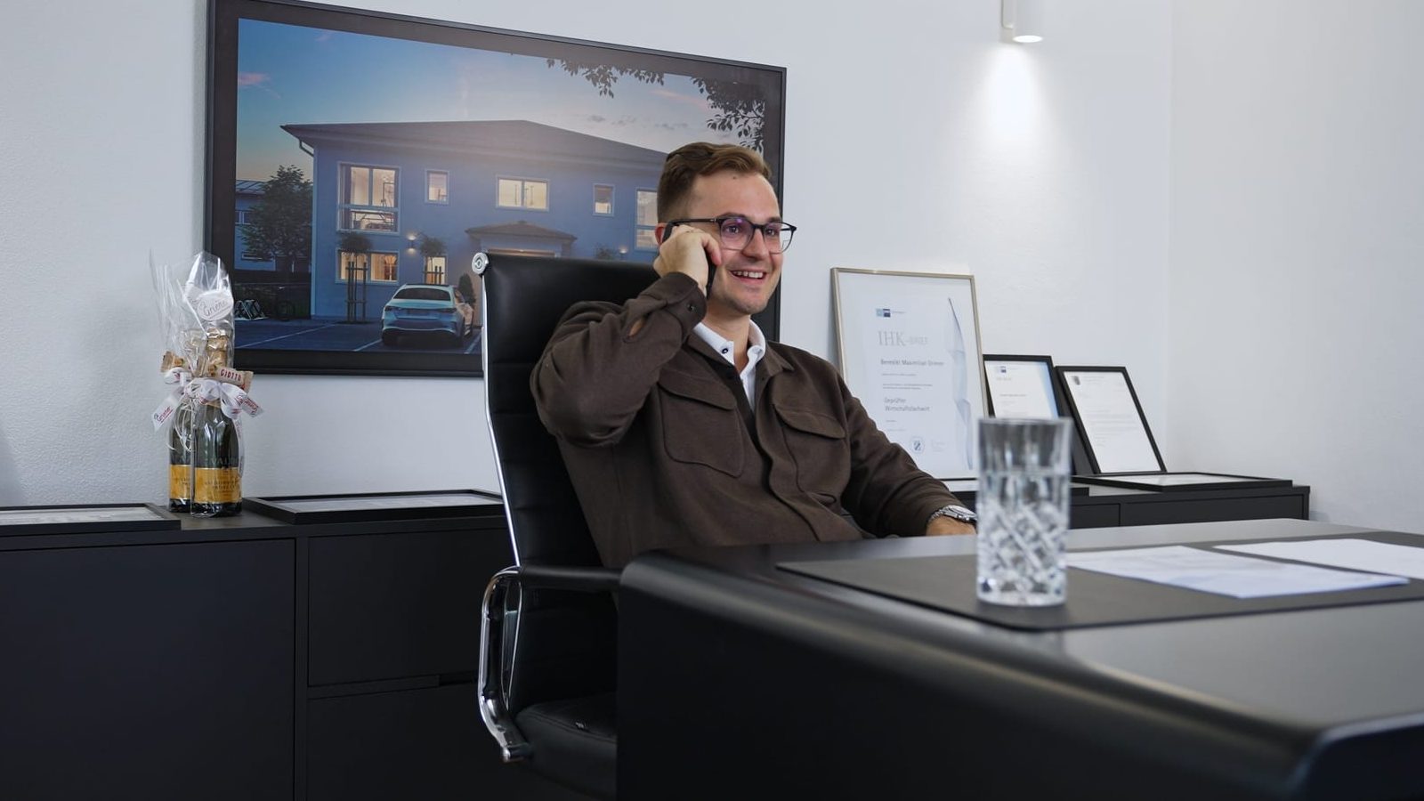 Benedikt Griener telefoniert am Schreibtisch im Büro und schaut freundlich in die Kamera
