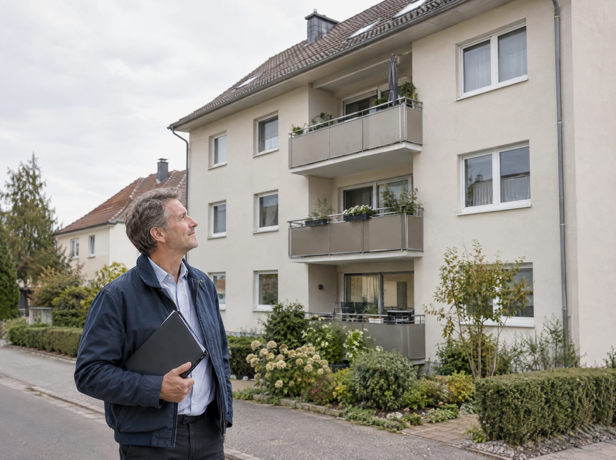 Eigentümer mit Mappe vor einem gepflegten Mehrfamilienhaus mit Balkonen